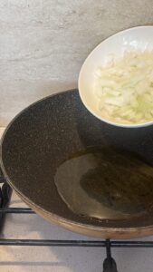 Oil heating in a hot skillet next to a bowl of chopped yellow onion, ready for the beef stir-fry