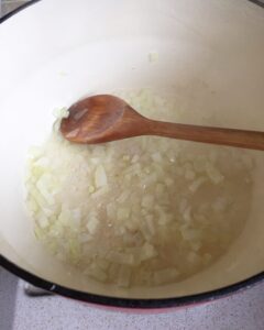 Chopped onions sautéing in a pot with a wooden spoon, the first step for making creamy tomato and red pepper soup.