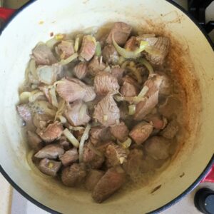 Chunks of beef and sliced onions browning in a Dutch oven