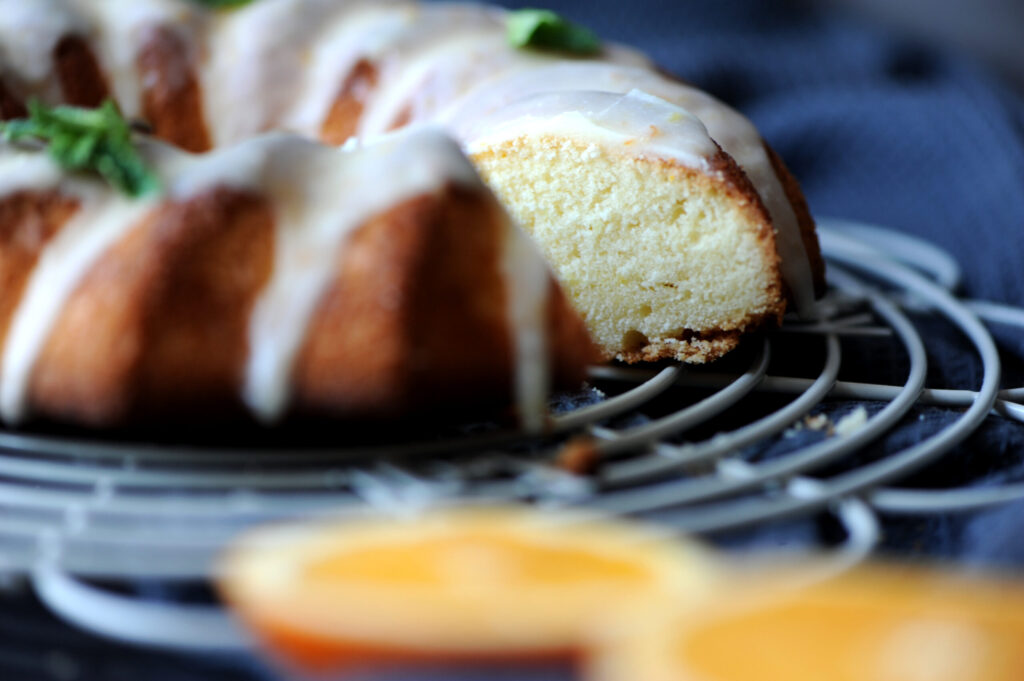A slice of lemon ginger bundt cake with dripping orange glaze on a wire cooling rack.