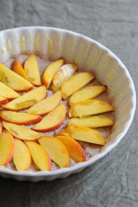 Preparing the cake pan with butter, sugar, and sliced peaches for a peach upside-down cake.