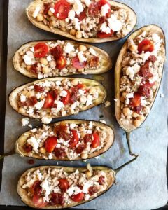 Unbaked eggplant boats stuffed with ground beef, chickpeas, cherry tomatoes, and feta on a baking sheet