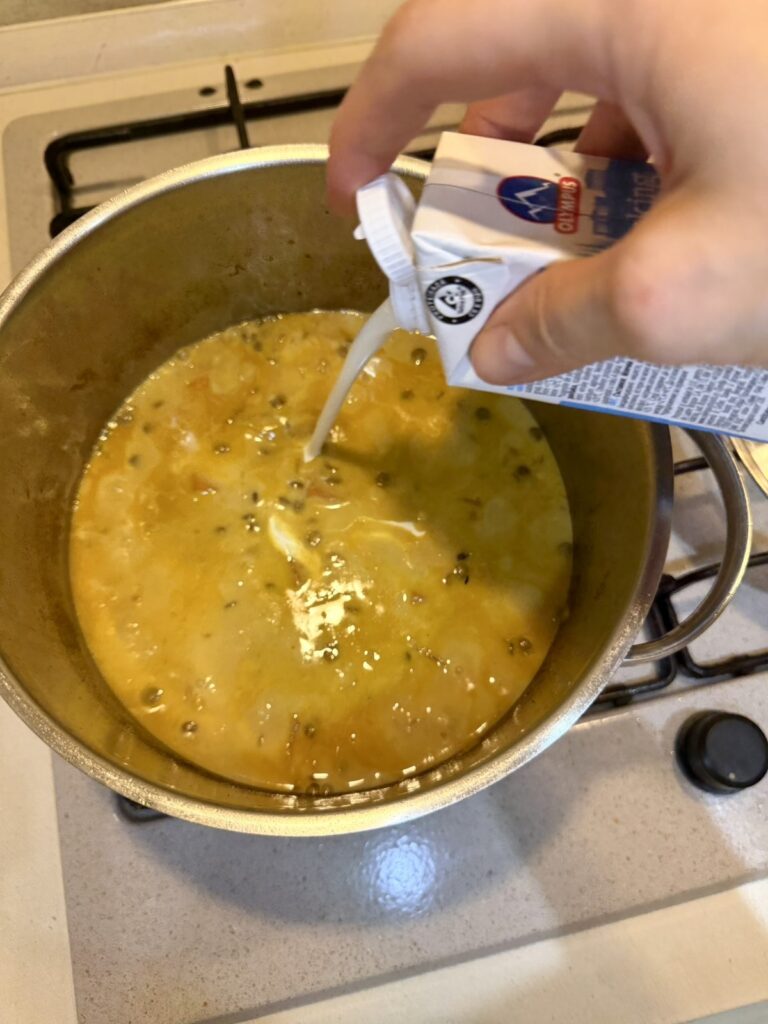 Light cream being poured into cooked green lentil soup