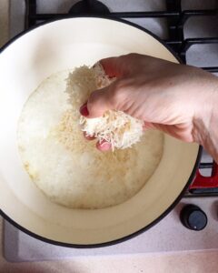Hand adding a handful of grated parmesan into the truffle cream sauce in a pot