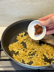 Adding Tom Yum paste to sautéed onions in a skillet.