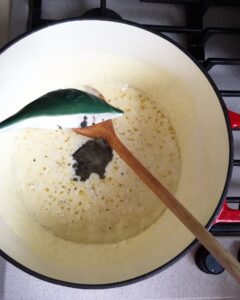 Adding a spoonful of black truffle paste into simmering cream sauce in a pot
