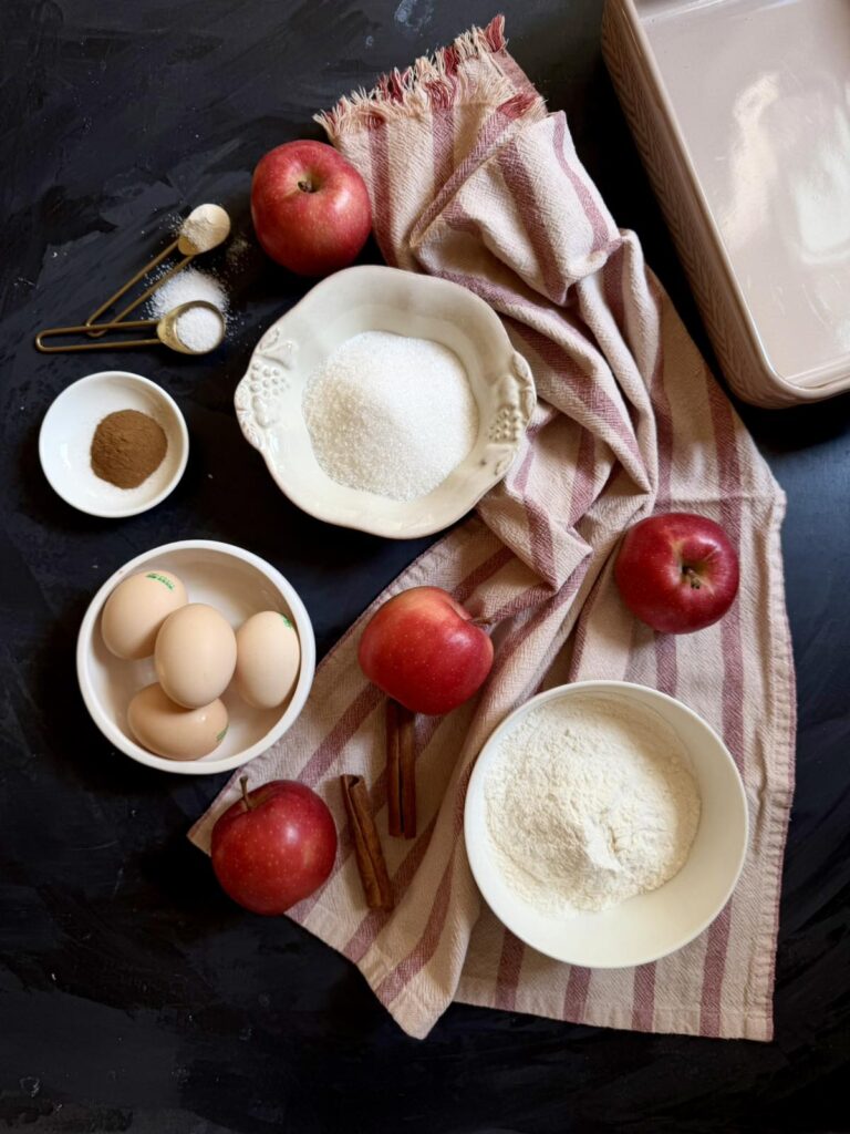 Overhead flat lay of apple charlotte cake ingredients including apples, eggs, and cinnamon