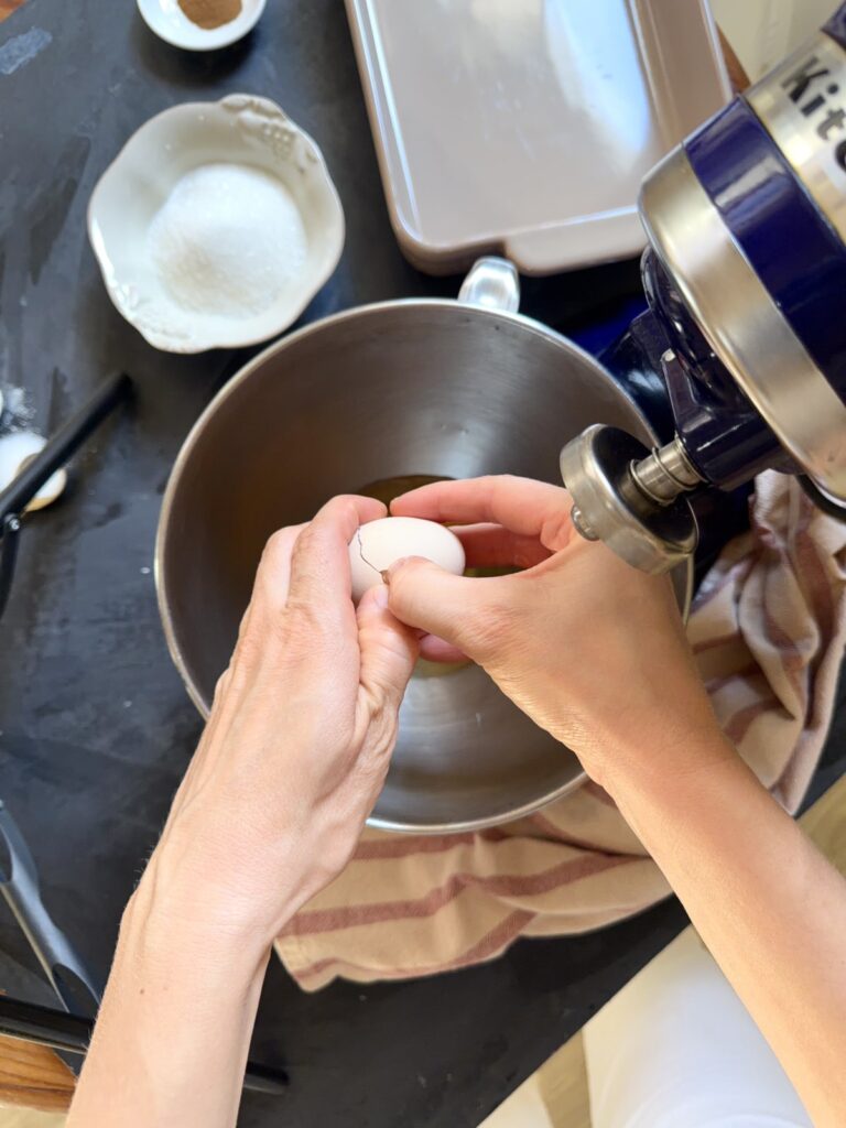 Cracking an egg into a stand mixer bowl to make apple charlotte cake batter