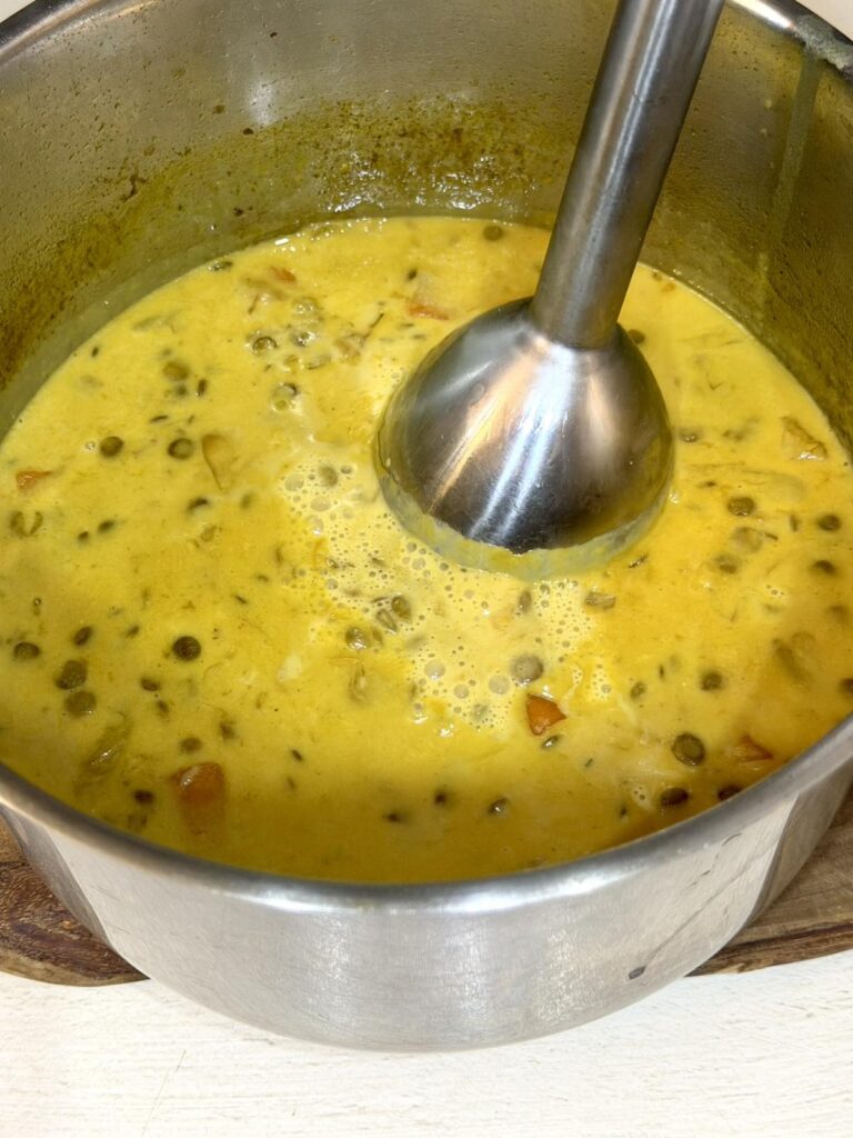 Green lentil soup being blended with an immersion blender