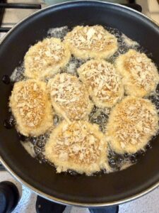 Breaded nuggets sizzling in hot oil in a black skillet.