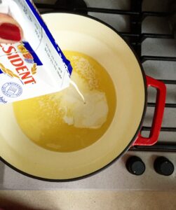 Pouring heavy cream into melted butter in a pot to start the truffle cream sauce