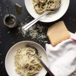 Two plates of creamy truffle pasta with parmesan styled with a parmesan wedge, a jar of truffle paste, and a linen napkin