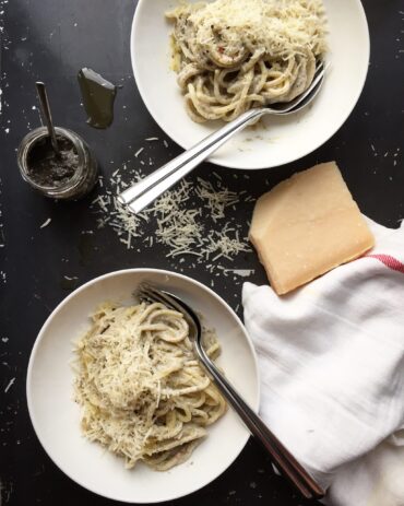 Two plates of creamy truffle pasta with parmesan styled with a parmesan wedge, a jar of truffle paste, and a linen napkin