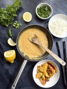 Skillet of coconut Tom Yum sauce with rice, cilantro, lemon, chili, and seared chicken.