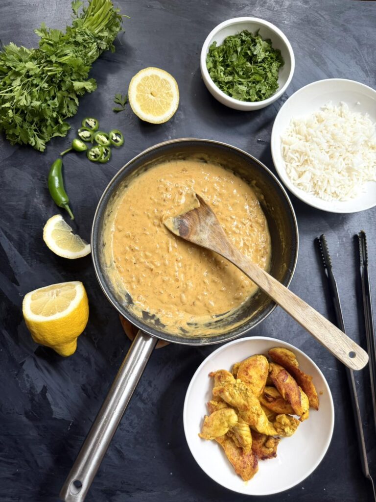Skillet of coconut Tom Yum sauce with rice, cilantro, lemon, chili, and seared chicken.