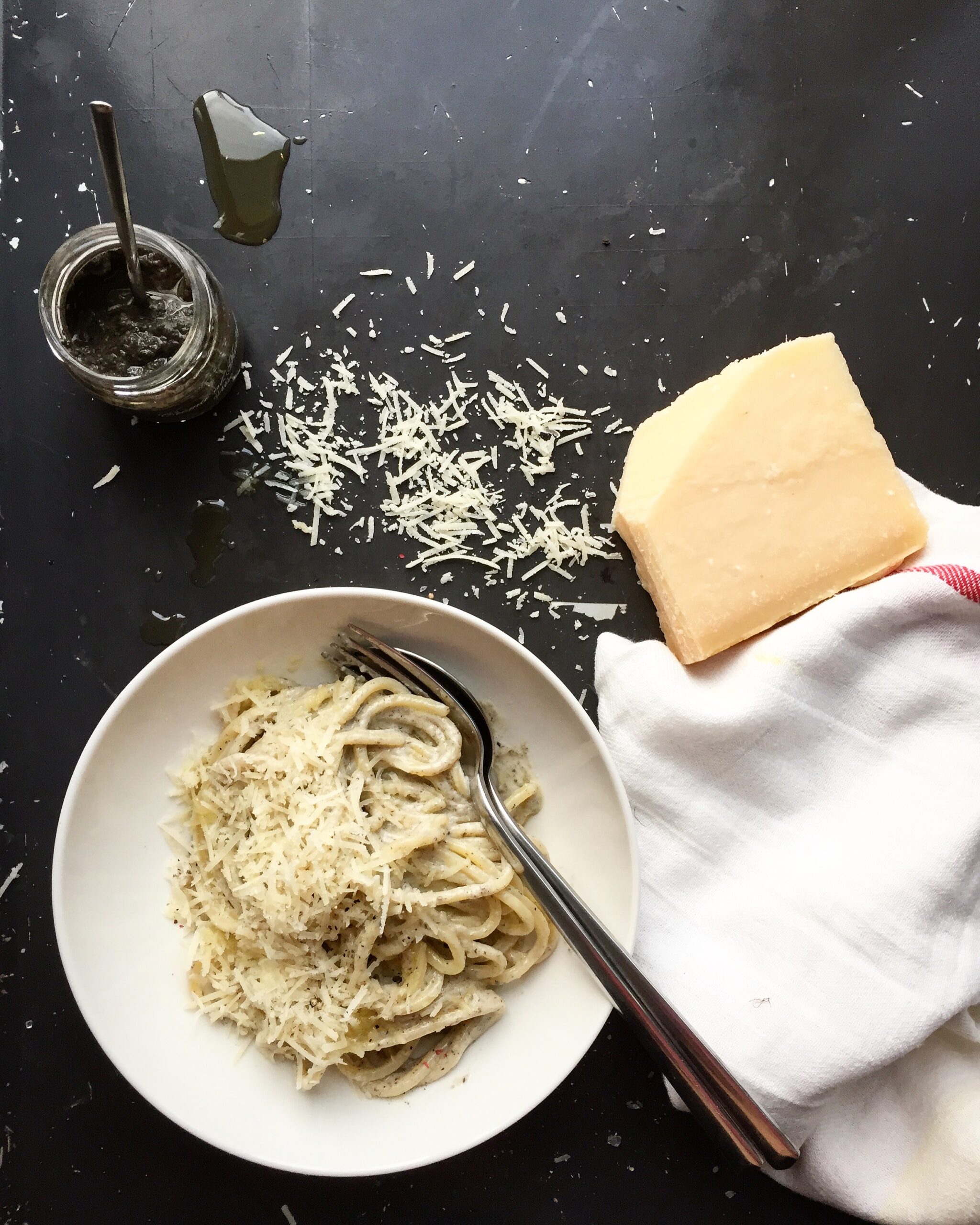 Bowl of creamy truffle pasta with parmesan on a dark background, styled with a parmesan wedge and jar of truffle paste