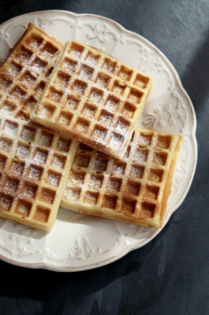 Easy Homemade Waffles topped with powdered sugar, served on a white patterned plate.