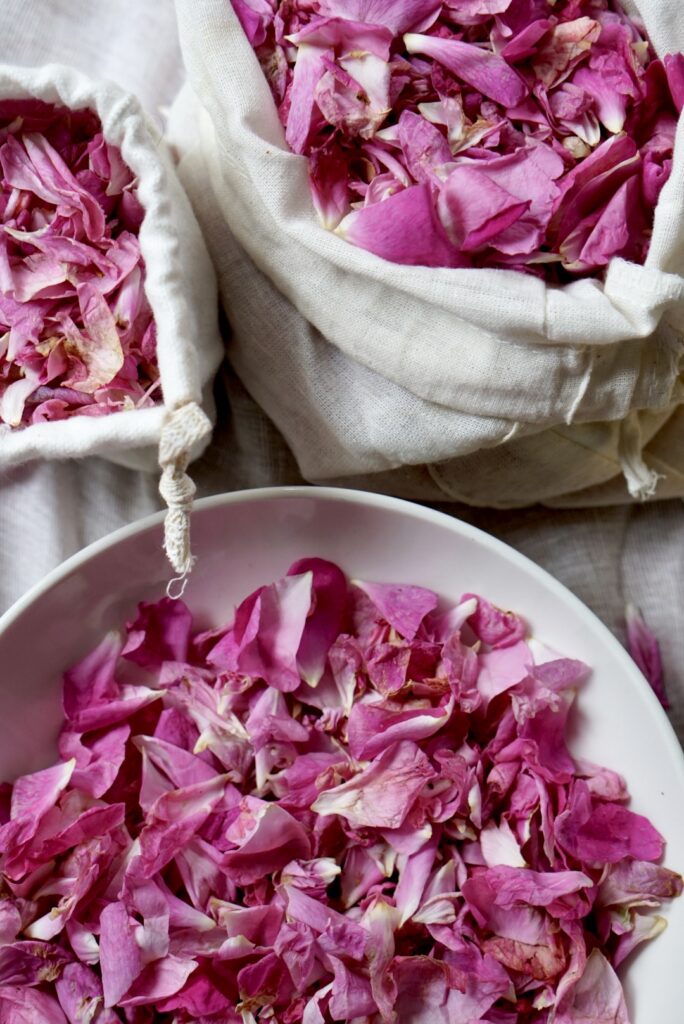 Close-up of fresh edible pink rose petals in a white bowl and a rustic linen bag for making rose petal jam