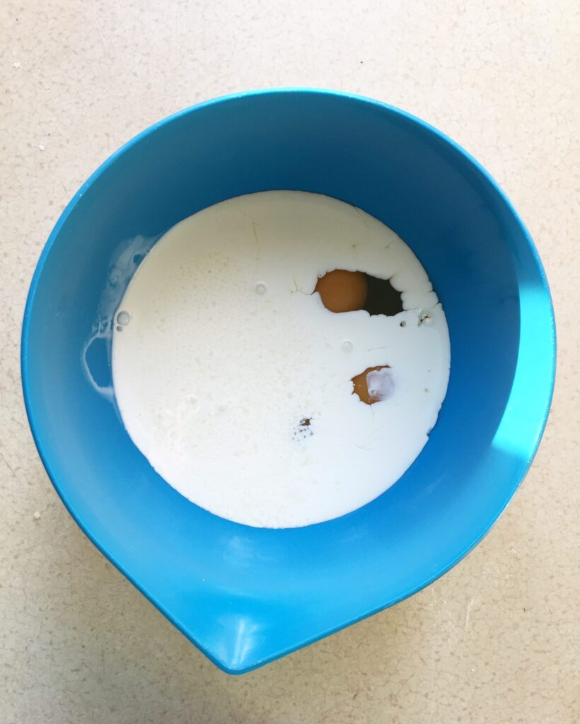 Egg cracked into cream in a bowl to make quiche custard