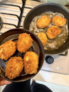 Golden fried chicken nuggets in a dish beside a skillet with the next batch cooking.