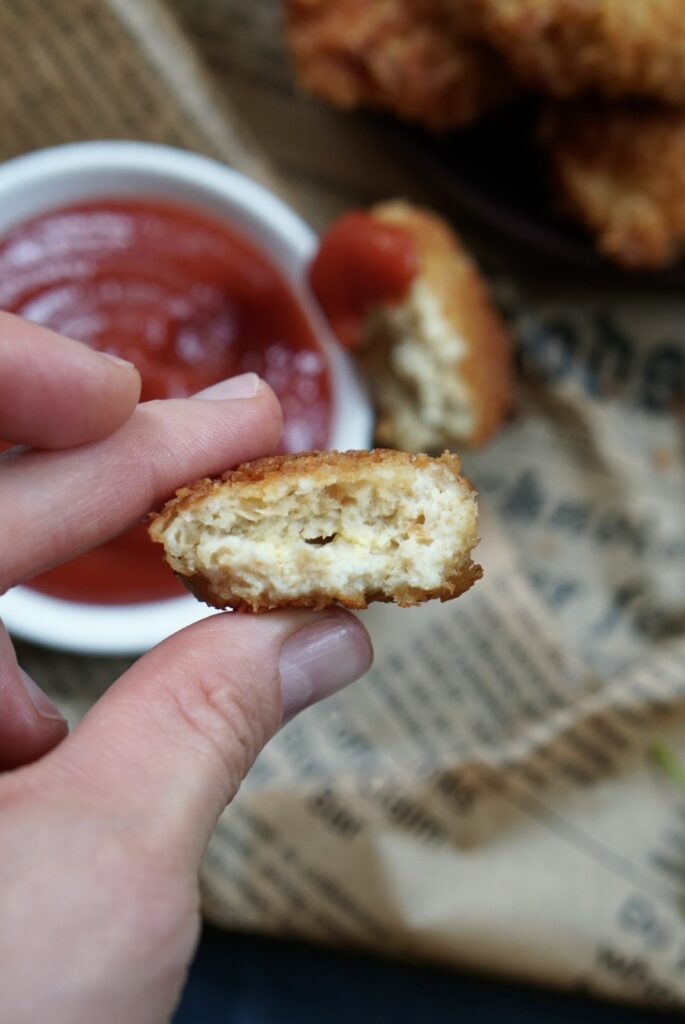 A hand holding a nugget broken in half to show the tender, cooked-through center.