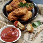 Crispy homemade chicken nuggets on a dark plate with parsley and a bowl of ketchup.