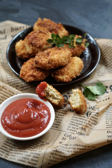 Crispy homemade chicken nuggets on a dark plate with parsley and a bowl of ketchup.