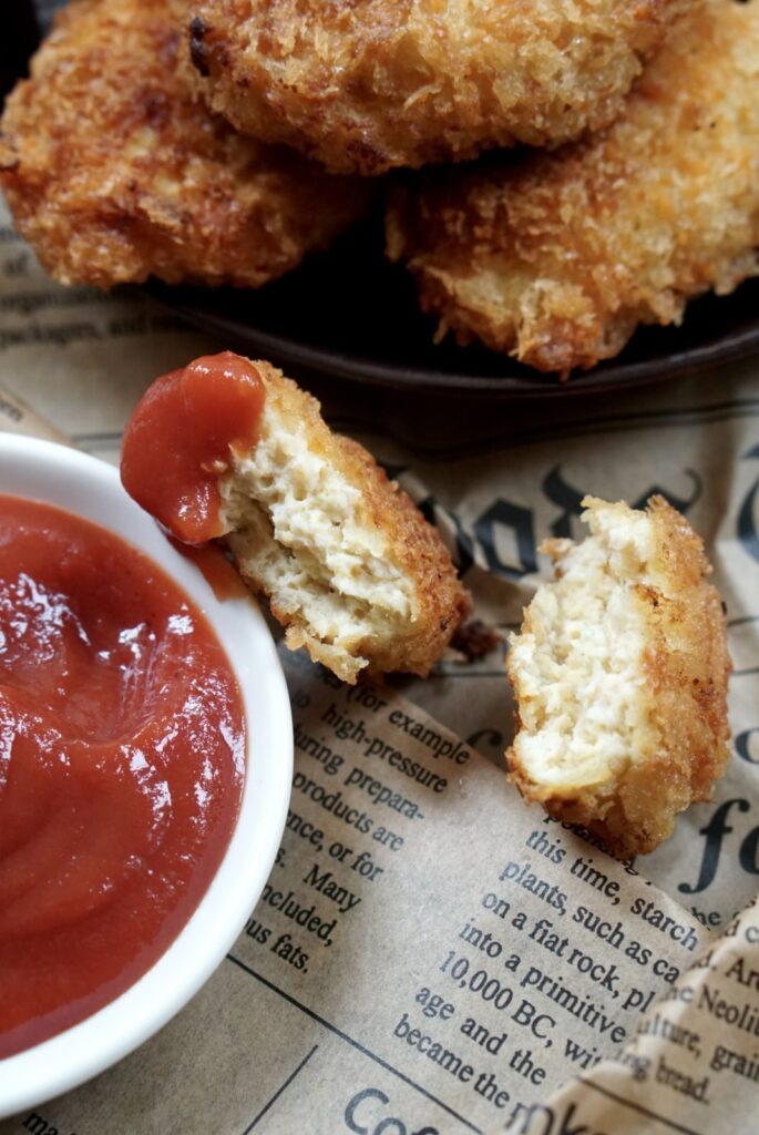 Close-up of crispy chicken nuggets with one broken open next to a bowl of ketchup.