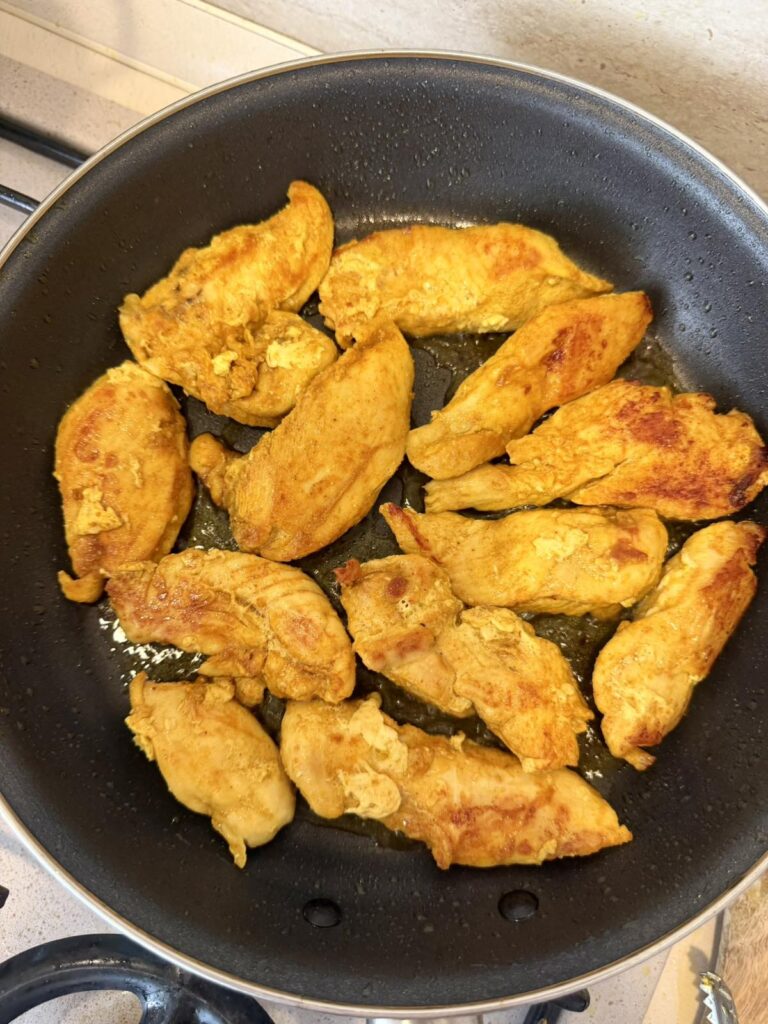 Seasoned chicken breast pieces searing in a skillet until golden brown.
