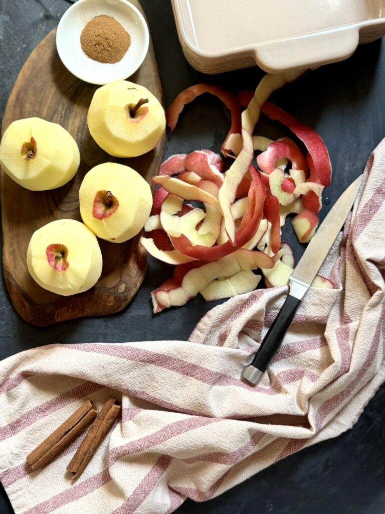 Peeled whole apples on a wooden board with apple peels and cinnamon sticks