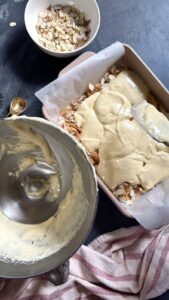 Pouring cake batter over a layer of apples and almonds in a baking pan