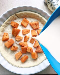 Pouring egg custard over roasted pumpkin cubes in a pie crust for pumpkin quiche
