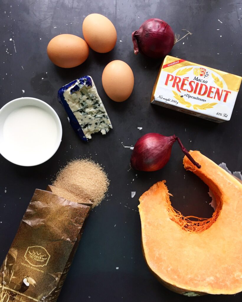 Flat lay of eggs, butter, blue cheese, cream, and red onion for pumpkin quiche