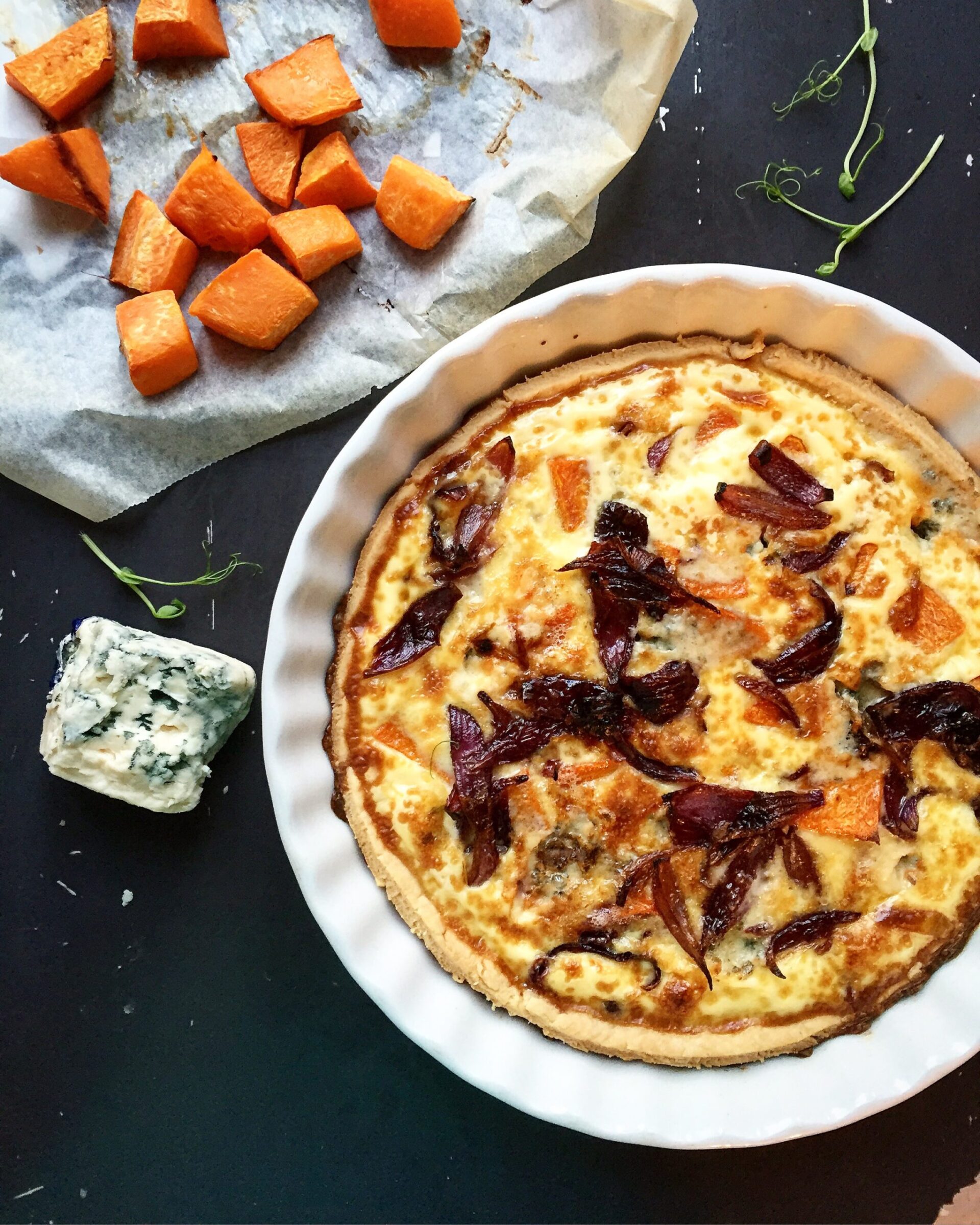 Baked pumpkin quiche with blue cheese and caramelized red onions, styled with roasted pumpkin cubes
