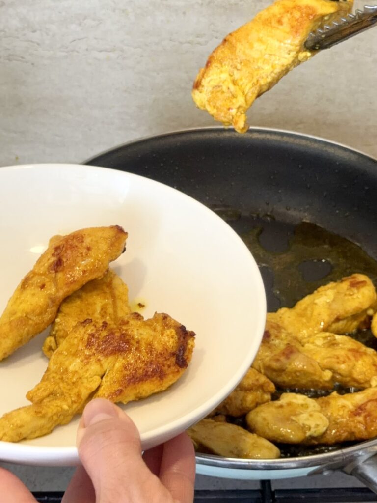 Removing golden seared chicken breast pieces from the skillet.