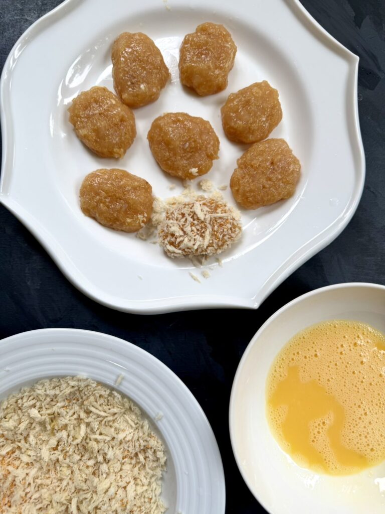 Raw shaped ground chicken nuggets on a white plate, one lightly dusted with crumbs.