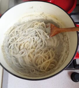 Cooked spaghetti being tossed with a wooden spoon in creamy truffle sauce in a pot