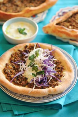 Turkish pide flatbread topped with ground beef and fresh cabbage salad, served with yogurt sauce