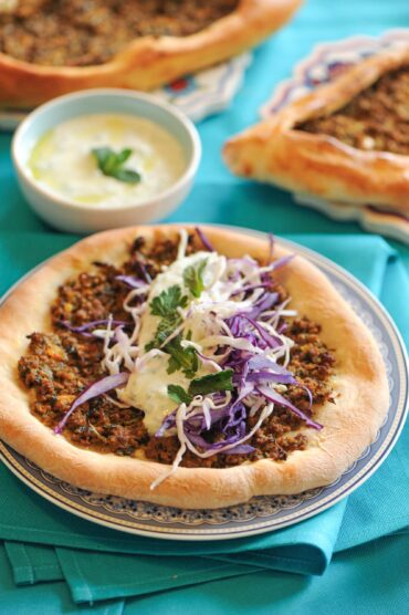 Turkish pide flatbread topped with ground beef and fresh cabbage salad, served with yogurt sauce
