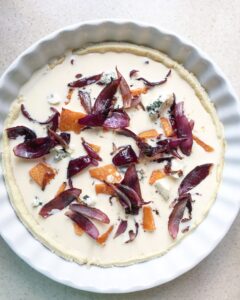 Unbaked pumpkin quiche topped with blue cheese and caramelized red onions