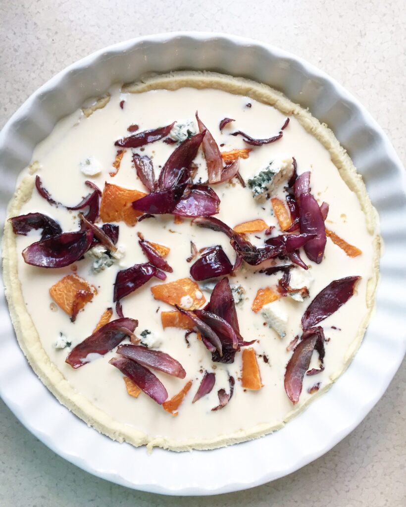 Unbaked pumpkin quiche topped with blue cheese and caramelized red onions