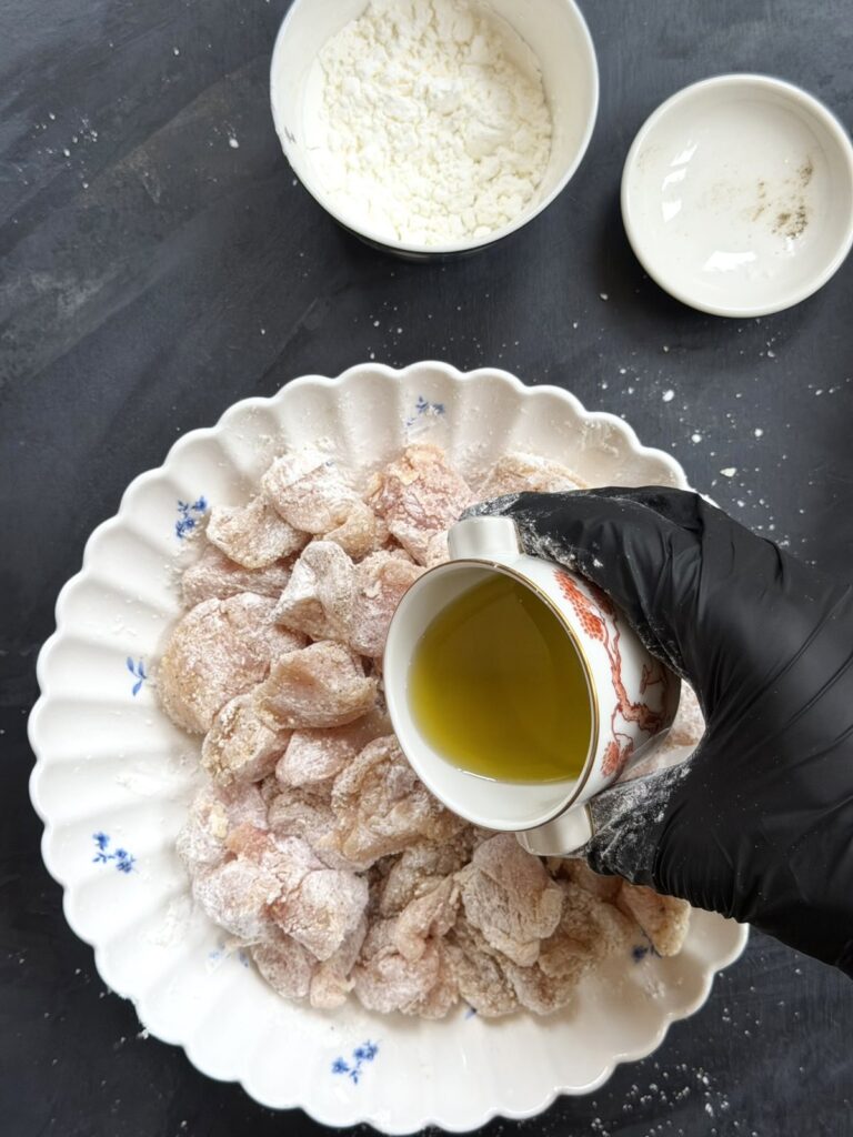 Pouring olive oil over cornstarch-coated chicken pieces in a bowl.