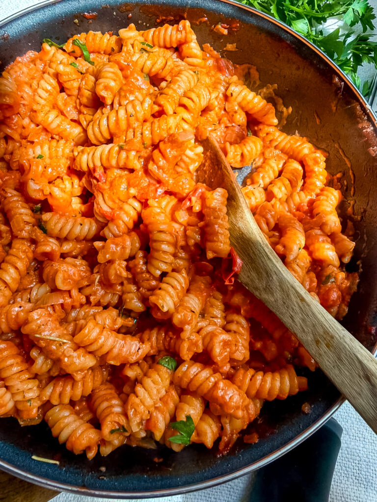 Fusilli pasta coated in creamy tomato sauce in a skillet with a wooden spoon.