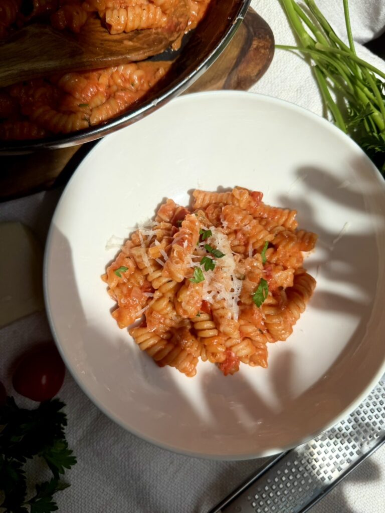 A white bowl of creamy tomato fusilli topped with grated Parmesan and parsley.