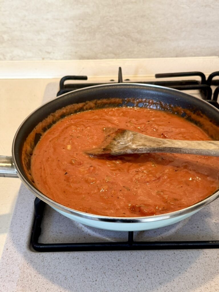 Creamy tomato sauce in a skillet on a gas stovetop with a wooden spoon.