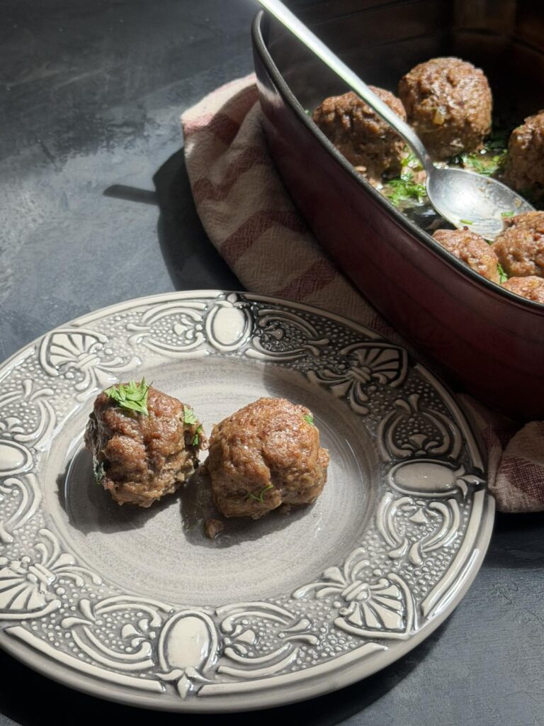 Two homemade baked beef patties on a decorative plate with a dish of patties in the background