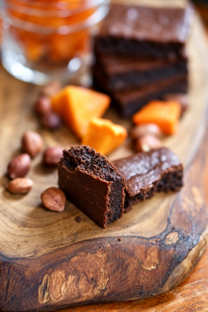 A broken chocolate pumpkin brownie showing its interior on a wooden board with pumpkin and hazelnuts