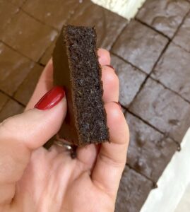 A hand holding a sliced pumpkin hazelnut brownie with more brownie squares on parchment paper behind it