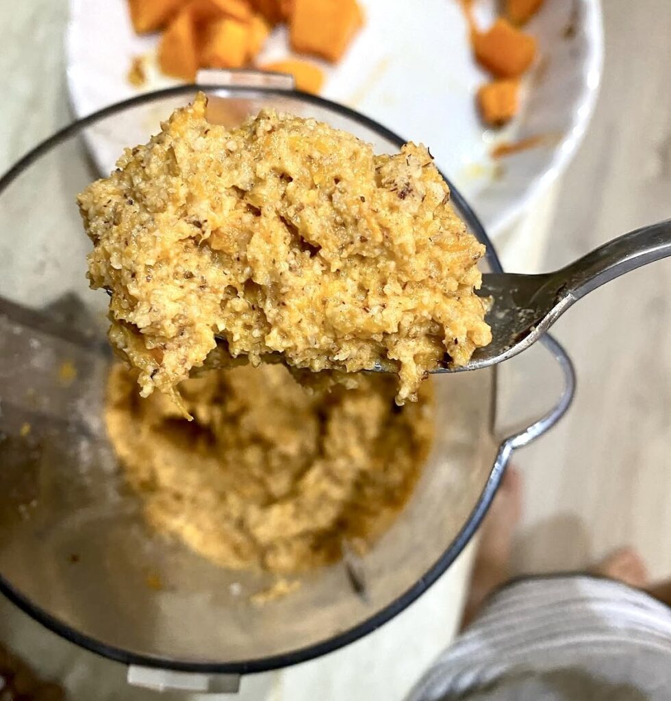 A spoonful of thick roasted pumpkin and ground hazelnut mixture above a blender jar