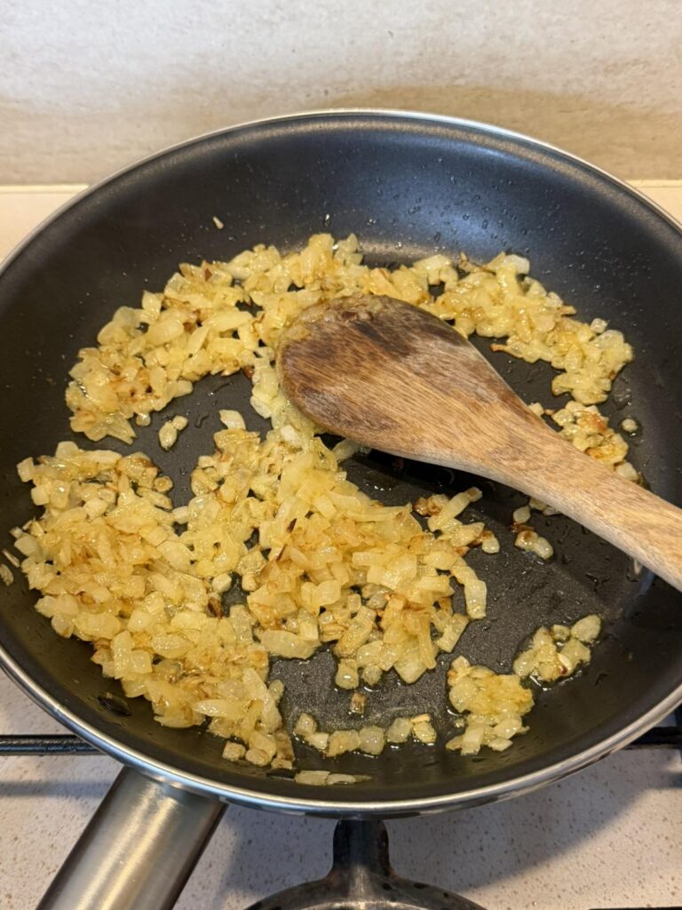Chopped onions sautéed until golden in a skillet with a wooden spoon
